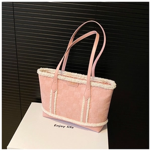 Close-up of pink tote bag with white plush trim and golden metal logo plaque detail