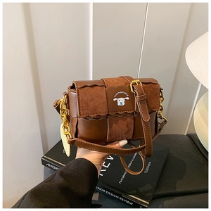 Détail du sac oreiller en cuir marron avec bord ondulé, emblème de chien et chaîne