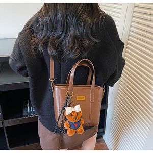 Close-up of brown bucket bag with plush bear charm and striped rope detail