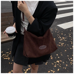 Detail of the brown suede tote bag featuring adjustable strap and embossed oval logo
