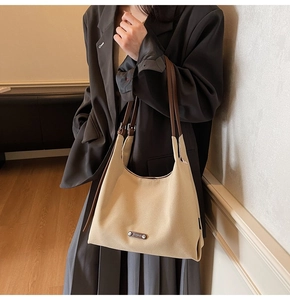 Detail of canvas tote bag showing brown leather strap and metal logo plaque on front