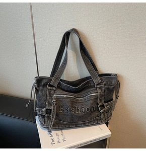 Detail of dark gray denim tote bag featuring embossed Fashion embroidery and side drawstrings