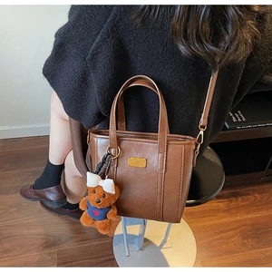 Detailed view of dark brown leather tote with golden plaque and teddy bear charm