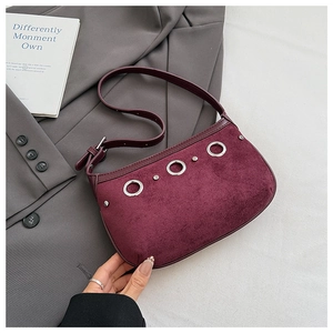 Close-up of burgundy suede shoulder bag with decorative metal rings and smooth strap