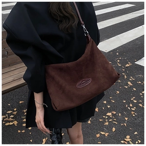 Detail of dark brown suede tote bag featuring oval embossed logo and long shoulder strap