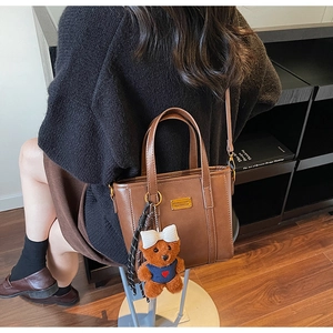 Close-up of brown vintage tote bag featuring a plush bear pendant and bow detail