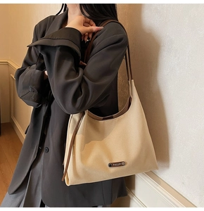 Detail view of beige canvas shoulder bag with brown leather trim on female model