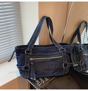Detail of dark blue denim tote bag featuring embossed logo and front zipper pocket