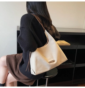 Detail of minimalist beige tote bag featuring a leather strap and branded metal logo plate