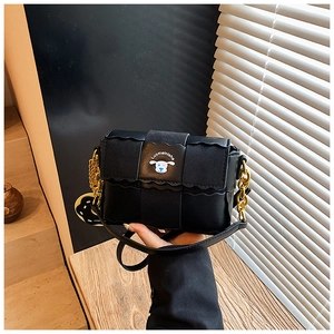 Détail du sac oreiller en cuir mat noir avec chaîne dorée et écusson chien de dessin animé