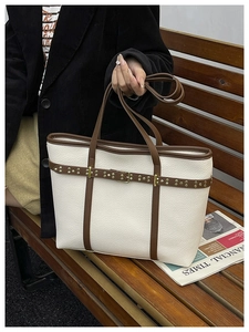 Macro shot of white pebble grain leather tote with brown trim and gold stud detail