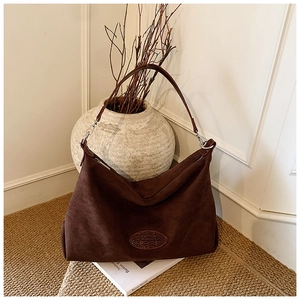 Close-up of deep brown suede hobo bag with embossed logo tag in a cozy home setting