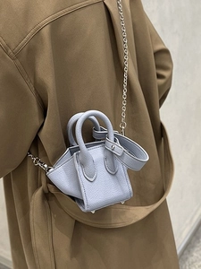 Chic light blue leather bucket bag with silver chain strap shown with a trench coat