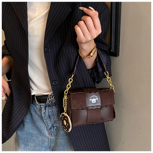 Sac bandoulière tissé marron avec chaîne dorée et breloque donut porté sur un blazer