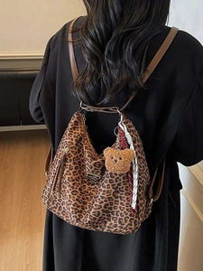 Chic leopard print tote bag with brown straps and plush bear charm shown on a model