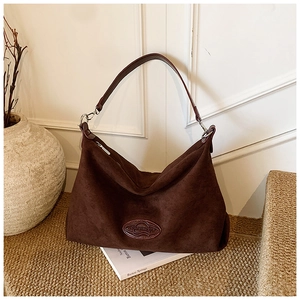 Macro shot of dark brown suede hobo bag with leather badge on a straw mat background