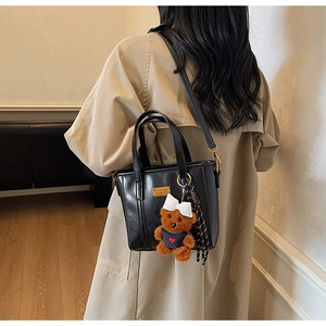 Detail of black vintage bucket bag with plush bear charm and adjustable crossbody strap