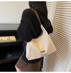 Detail view of cream shoulder bag with brown strap and metal plaque in a modern setting