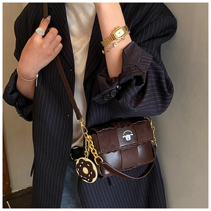 Détail du sac oreiller tressé marron foncé avec écusson chiot et breloque doughnut