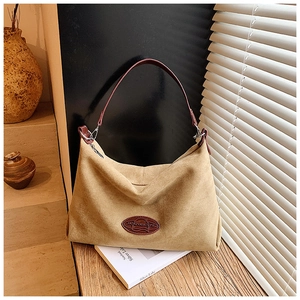 Detailed close-up of large camel suede hobo bag with leather logo patch and metal buckle