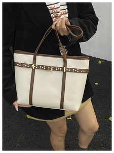 Detail of white lychee leather tote with silver rivets and brown trim on a handheld bag