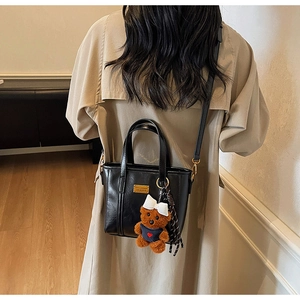 Detail of matte black PU leather bucket bag with cute brown plush bear charm and gold hardware