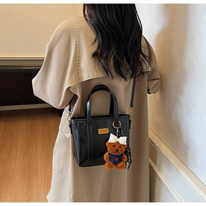 Detail of black leather bucket bag with gold logo and plush bear charm on a model