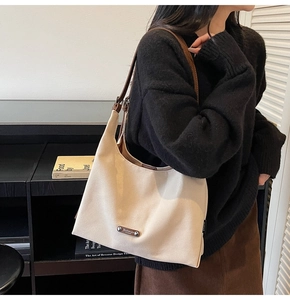 Detail of canvas shoulder bag with premium metal logo plate and brown leather strap