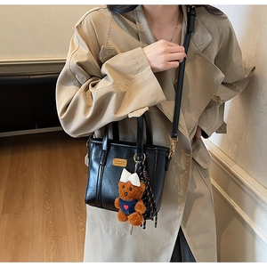 Detail of black leather handbag with a cute brown bear charm on khaki trench coat