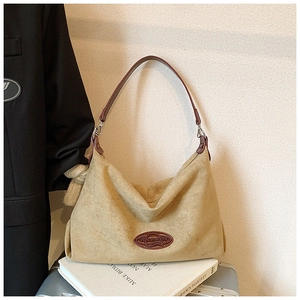Detail of khaki faux suede hobo bag featuring burgundy leather logo patch and artistic books