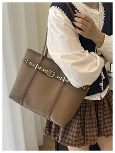 Detail view of brown pebbled leather tote bag with gold studs and belt buckle design