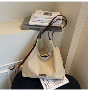 Detailed close-up of a cream canvas tote bag with a metallic logo plate and leather strap