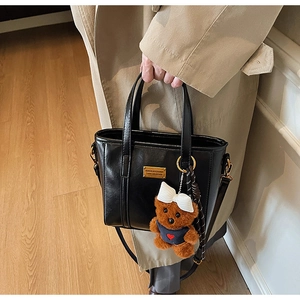 Detailed side view of black PU leather bucket bag with golden buckle and plush bear charm
