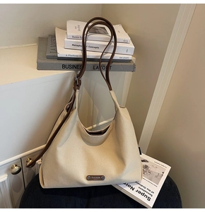 Detailed shot of a minimalist hobo shoulder bag with a metal brand plate on off-white canvas
