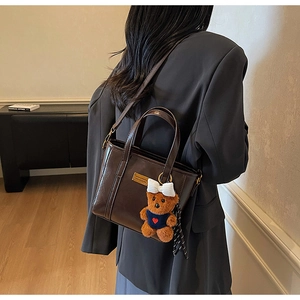 Detail of dark brown vintage bucket bag with plush bear charm and golden hardware