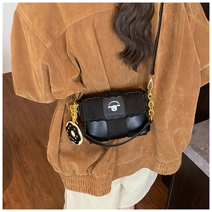 Detail of black crossbody bag with scalloped edges, cartoon embroidery, and charm pendant