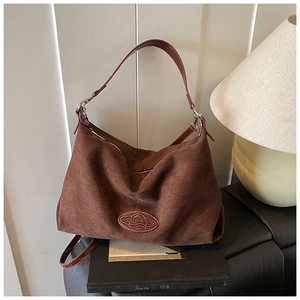 Detail of dark brown suede shoulder bag with oval logo plaque and wide strap handle