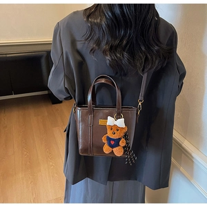 Detail of dark brown tote bag featuring a cute teddy bear pendant and a golden plaque