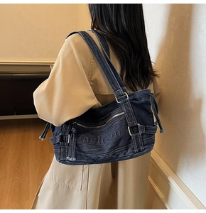 Detail view of a navy denim tote bag with Fashion embossing and metal zip accents