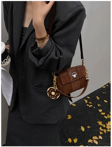 Détail du sac bandoulière marron avec chaîne dorée et breloque donut sur costume