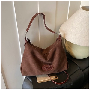 Detailed view of the dark brown matte suede tote bag with logo on a black leather bench