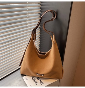 Close-up of camel canvas tote bag with brown leather strap and metal logo plate detail