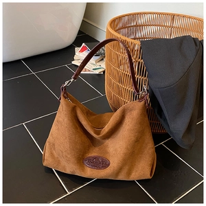Detail of a brown suede hobo bag with leather handles on a modern marble floor