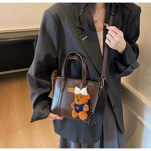 Detail of dark brown polished leather bucket bag with logo plate and teddy bear charm