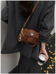 Détail d'un sac bandoulière marron avec logo chien et pendentif doré en forme de donut