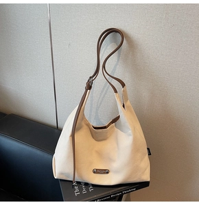 Detail of off-white canvas hobo bag with brown leather strap and brand nameplate