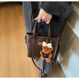 Close-up of vintage brown tote bag with golden metal plaque and cute bear charm