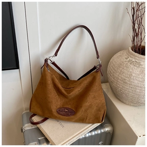 Detail of caramel suede bag on vintage suitcase with red leather patch and dual straps