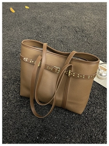 Close-up of brown pebbled leather tote bag with gold rivets on asphalt surface