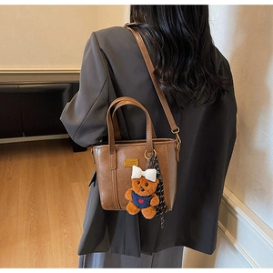 Detail view of brown vintage tote bag with plush bear charm and silk scarf decoration